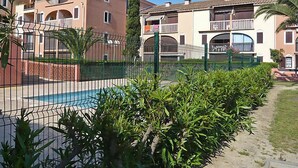 Edificio residencial con piscina, rodeado de vegetación y una valla metálica.