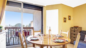 Un comedor con una mesa dispuesta para cuatro, sillas, un sofá y una puerta corrediza de vidrio que da a un balcón.