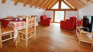 A cozy attic room with a dining table, chairs, a sofa, and a TV. - Albergo Diffuso - Cjasa de Barce by Interhome (Barcis Lake)
