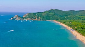 Eine Küstenlandschaft mit Strand, Booten und einem Hügel, der eine Struktur trägt.