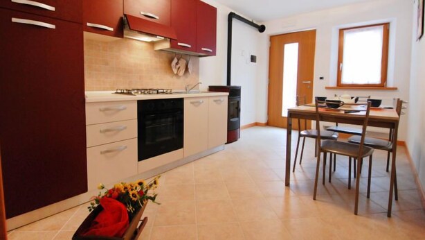 A compact kitchen with a dining area, featuring a stove, oven, and a dining table with chairs. - Albergo Diffuso - Cjasa Marisa by Interhome (Barcis Lake)