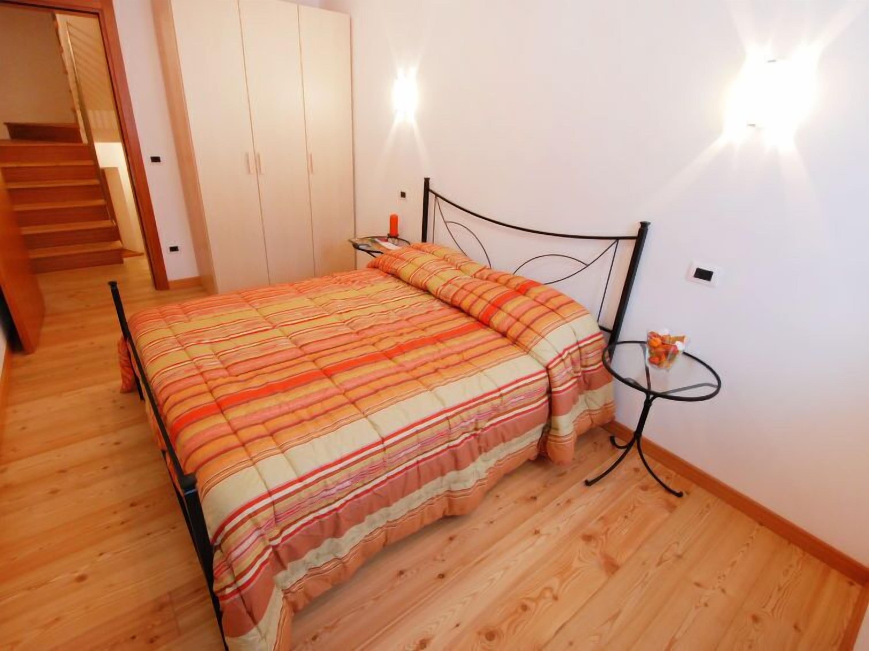 Een slaapkamer met een bed, houten vloeren, een nachtkastje en een wandlamp.