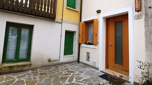 A courtyard with a stone floor, a wooden balcony, and a door with a number plate. - Albergo Diffuso - Cjasa Marisa by Interhome (Barcis Lake)