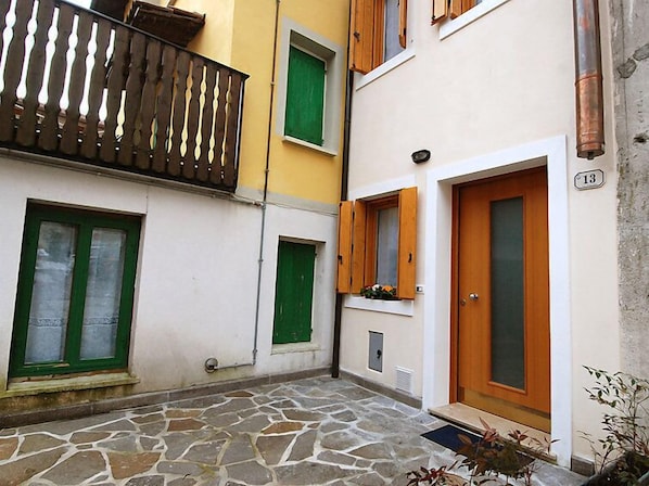 A courtyard with a stone floor, a wooden balcony, and a door with a number plate.