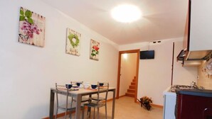 A dining area with a table and chairs, a kitchen with a stove, and a staircase leading to another room. - Albergo Diffuso - Cjasa Marisa by Interhome (Barcis Lake)