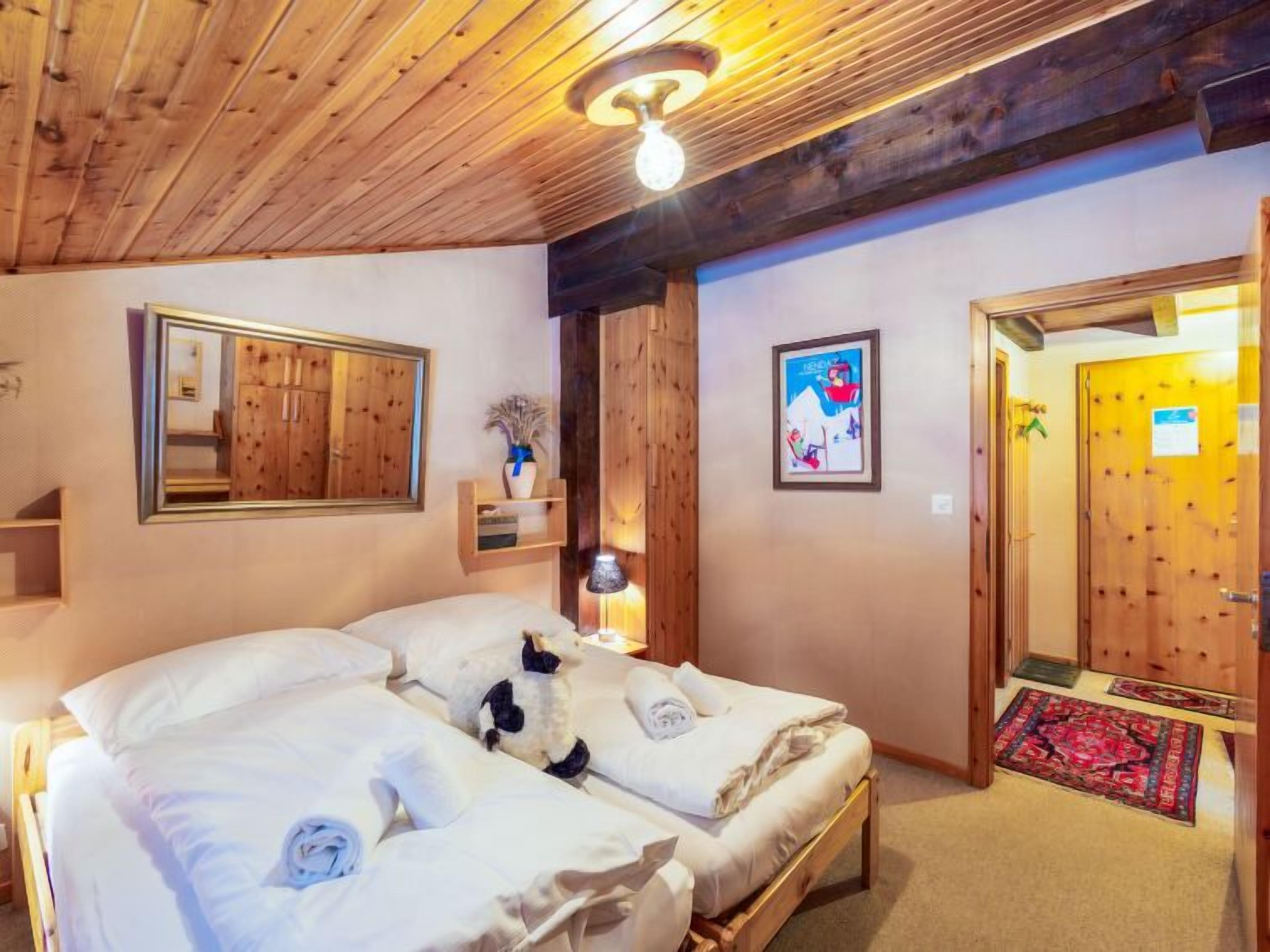 Una habitación con dos camas, techo de madera, un espejo, un cuadro enmarco y una puerta con felpudo.