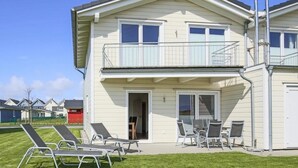 Ein zweistöckiges Haus mit einem Balkon, einer überdachten Veranda mit Stühlen und Tisch sowie einem Rasen mit Liegestühlen.