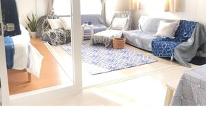 Un salon lumineux avec un canapé, une petite table et un lampadaire. On y trouve une plante et une fenêtre avec des rideaux.