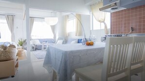 Une pièce moderne et bien éclairée, comprenant une table à manger, des chaises, un coin cuisine et offrant une vue sur l’extérieur.
