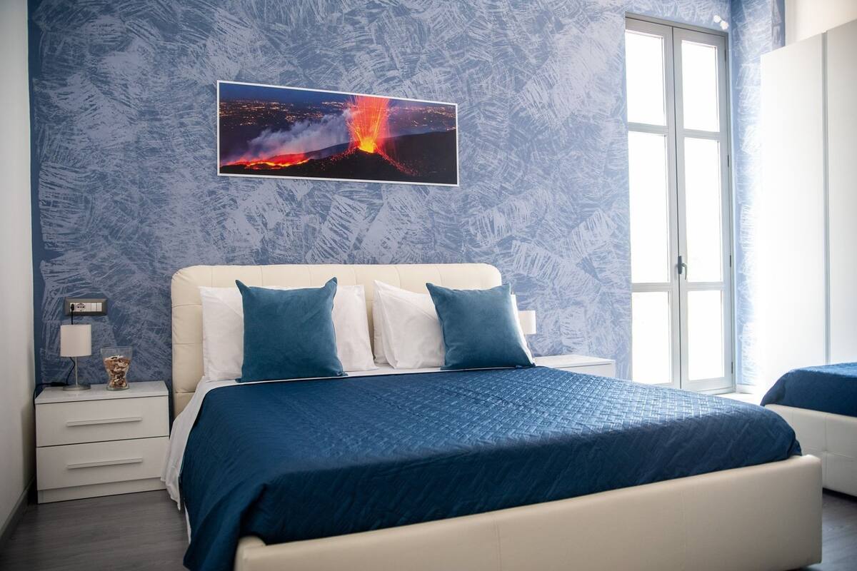 Un dormitorio con una cama, una mesita de noche, una lámpara y una ventana.