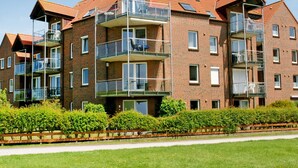 Un edificio de apartamentos de varios pisos de ladrillo, con balcones, un camino pavimentado y abundante vegetación bien cuidada.