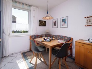Et spiseområde med et træbord, fire stole, en hængende lampe og et vindue med gardiner.