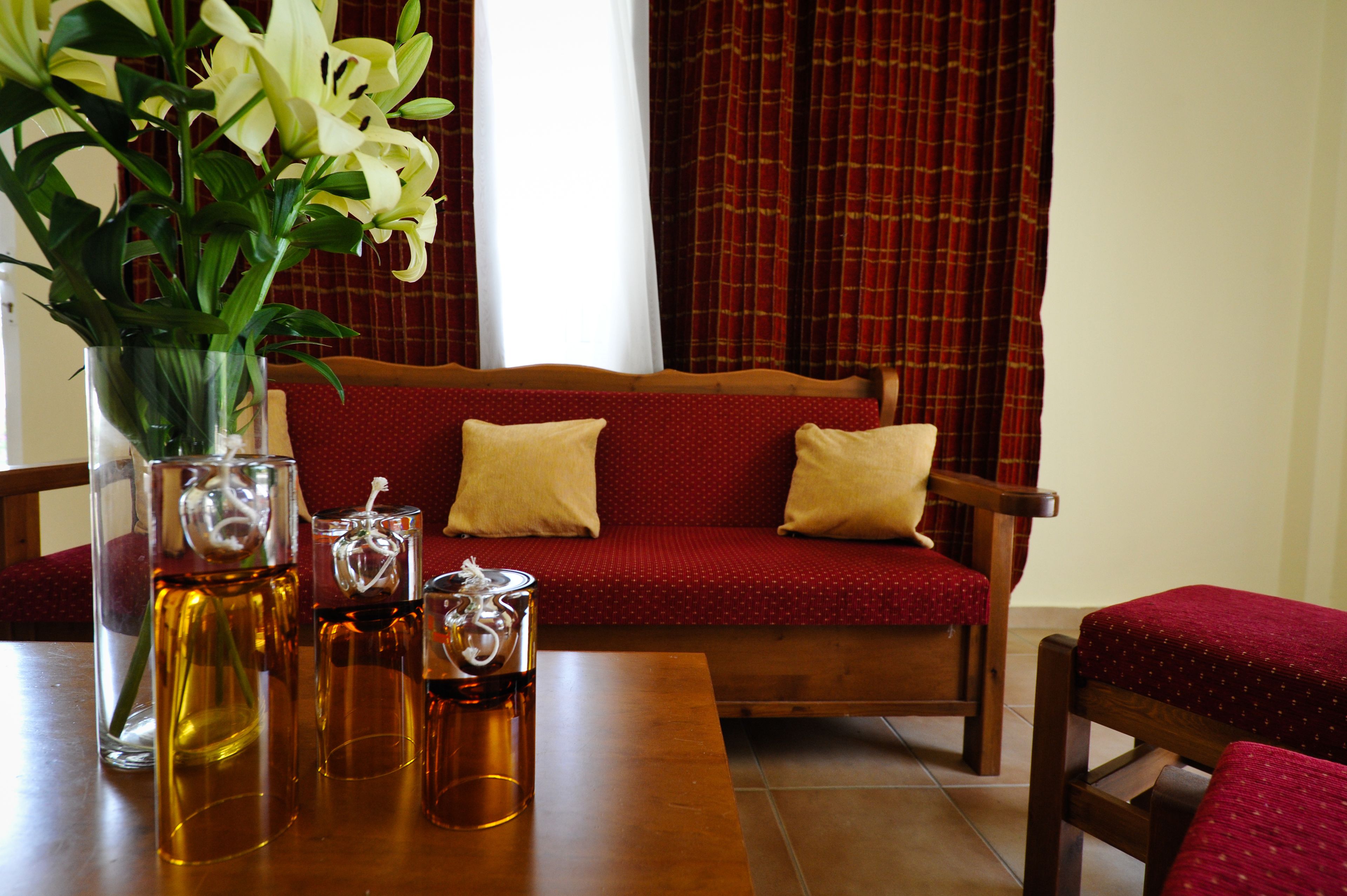 Ein Essbereich mit einem Holztisch, klaren Glasvasen mit Blumen und einem roten, gepolsterten Sofa mit Kissen.