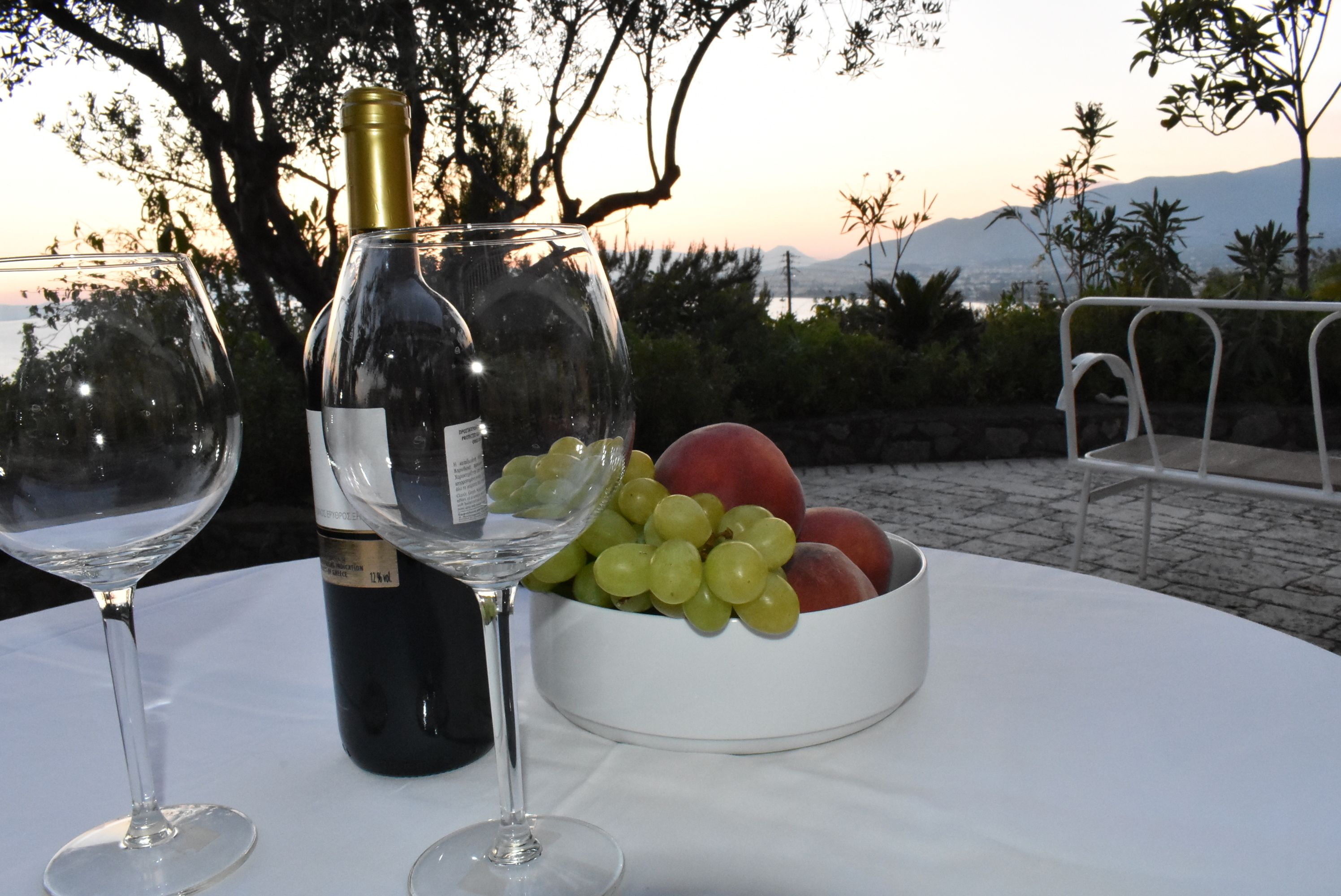 Una mesa con una botella de vino, dos copas de vino y un bol de fruta.