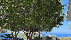 A paved outdoor area with a car parked under a tree, a bench, and a table with a chair. - Verga Apartments & Suites (Kalamata)