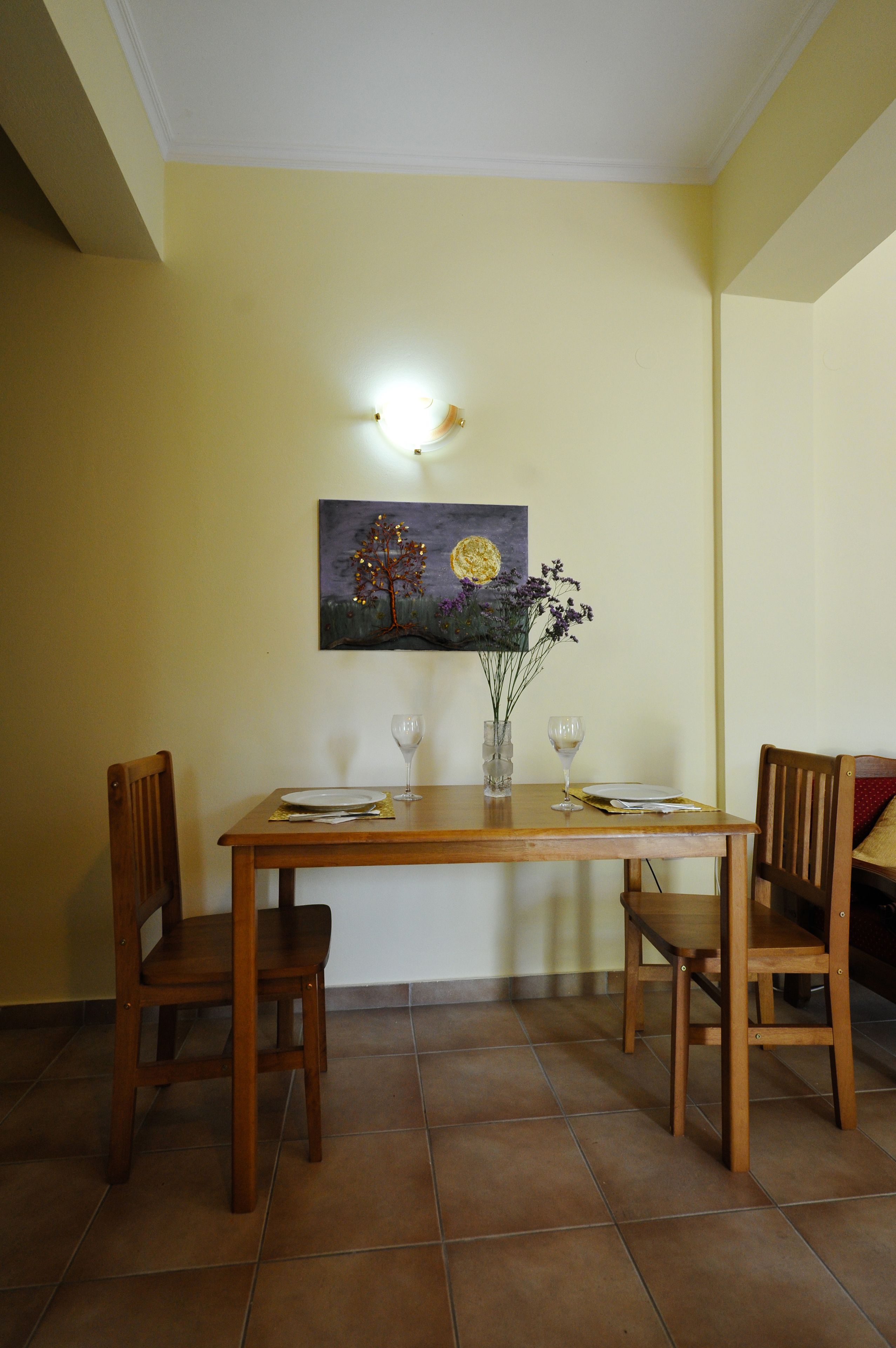 A dining table with chairs, a vase with flowers, and a painting on the wall.