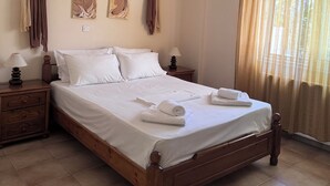 A neatly made bed with white linens, a wooden headboard, and a nightstand with a lamp. - Verga Apartments & Suites (Kalamata)