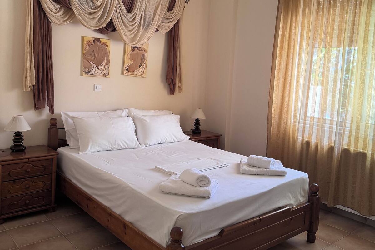 A neatly made bed with white linens, a wooden headboard, and a nightstand with a lamp.