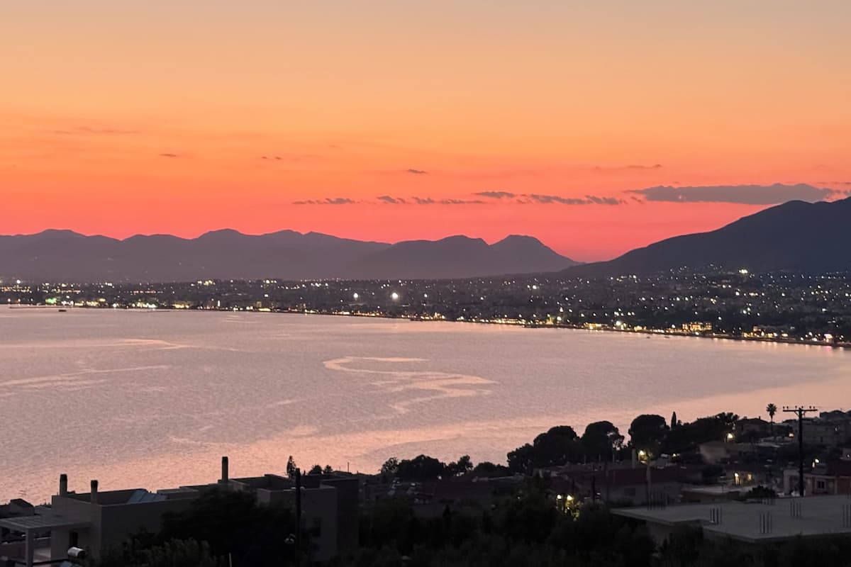 A coastal cityscape at sunset with a view of the water and distant mountains.