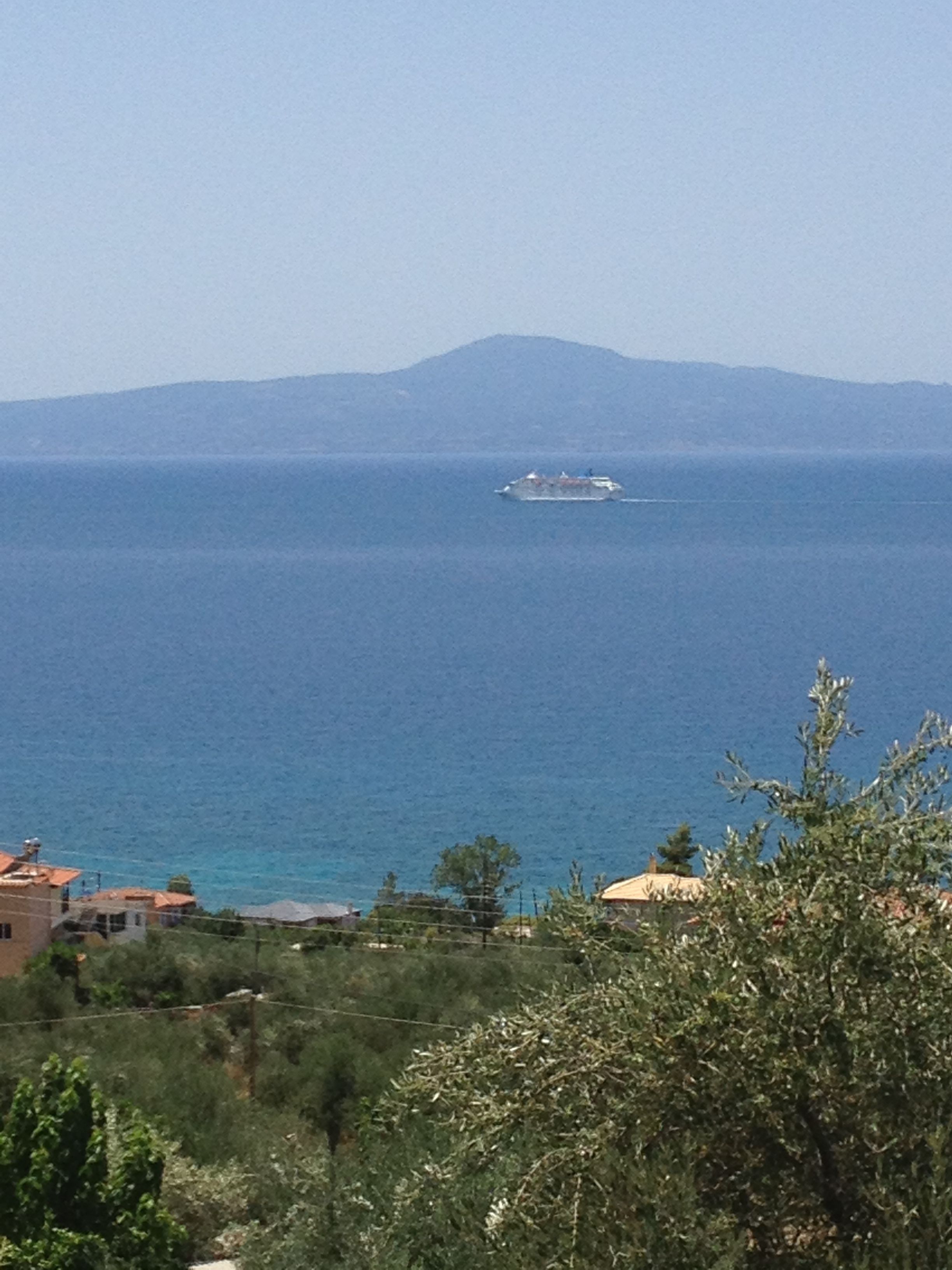 Vista costera con un barco a lo lejos, edificios y montañas.
