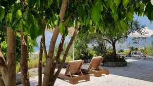 A sunlit outdoor seating area with wooden lounge chairs, surrounded by trees and a view of the cityscape. - Verga Apartments & Suites (Kalamata)