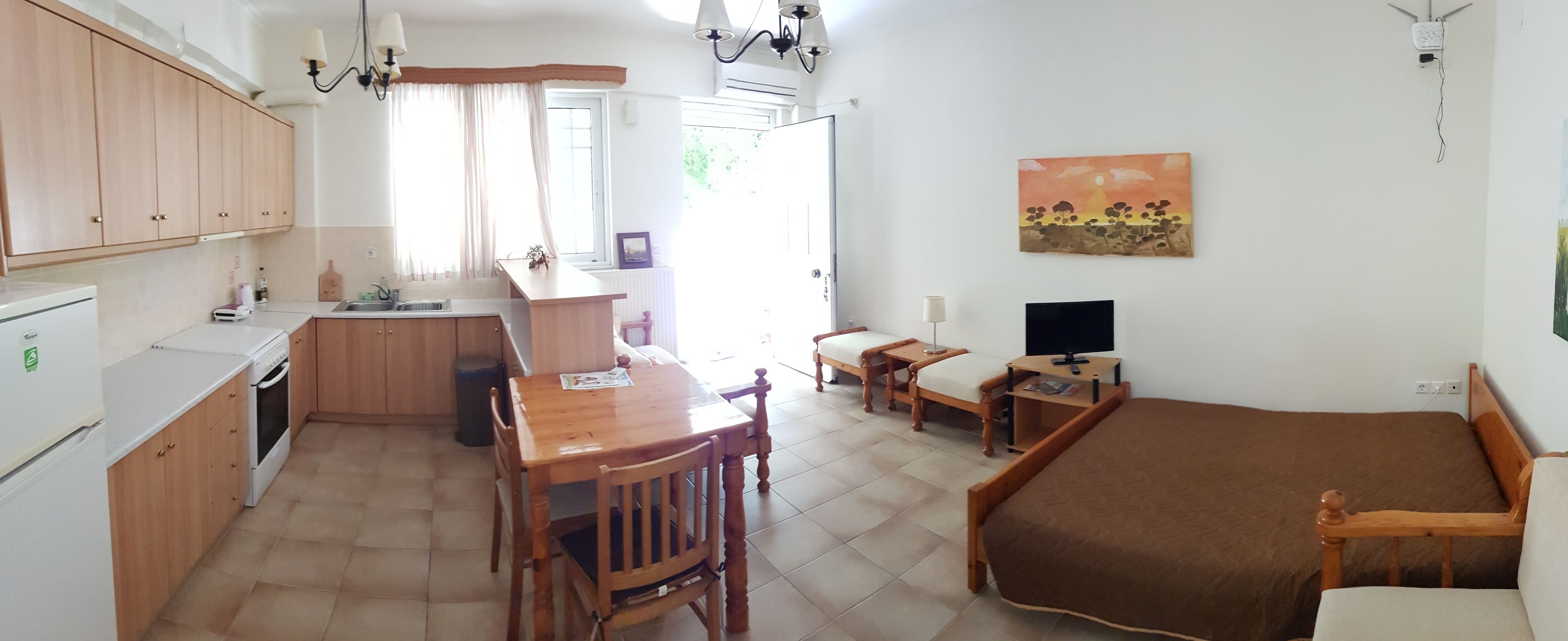A compact kitchen with a dining area, a single bed, and a TV.