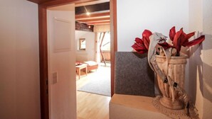 A hallway with a wooden door leading to a room with a bed and a small table. There is a vase with red flowers on a table in the hallway. - Beim Holzschnitzer by Interhome (Sölden)