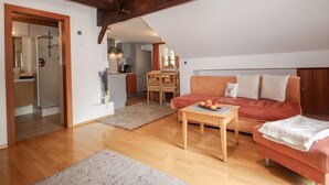 A cozy loft-style living space with a wooden ceiling, a red sofa, a wooden coffee table, and a kitchen in the background. - Beim Holzschnitzer by Interhome (Sölden)