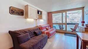 Un soggiorno accogliente con un divano marrone, un poggiapiedi decorato, mobili in legno e una grande finestra che si affaccia su un paesaggio innevato.