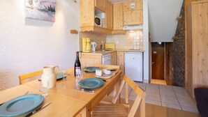 Una cucina compatta con mobili in legno, un piccolo frigorifero e un tavolo da pranzo per due persone.