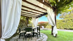 A covered outdoor seating area with stone flooring and white curtains. - Stefano by Interhome (Forte dei Marmi)