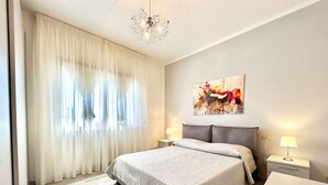 A modern bedroom with a large bed, two bedside tables with lamps, a chandelier, and a painting on the wall. - Stefano by Interhome (Forte dei Marmi)