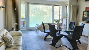 Un soggiorno moderno con un tavolo in vetro, sedie nere, un divano bianco e vista su un lago attraverso ampie finestre.