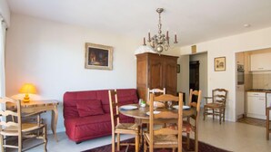 Un coin repas avec une table ronde, des chaises en bois, un canapé rouge, un lustre et, au fond, une cuisine.