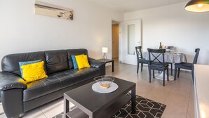 Een moderne woonkamer met een zwarte leren bank, een klein bijzettafeltje en een eethoek met tafel en stoelen.