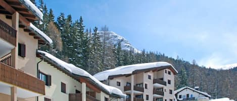 Un hotel de varios pisos con balcones, techos nevados y montañas al fondo.