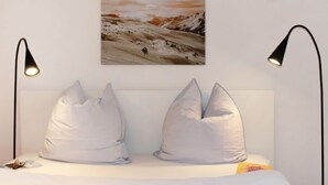 A bedroom with a bed, two pillows, a painting, and two wall-mounted lamps. - Residenza Chesa Margun 35-5 by Interhome (Silvaplana-Surlej)