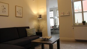A living room with a dark sofa, a coffee table with a decorative bowl, a floor lamp, and framed artwork on the wall. - Altstadt Villa Wohnung 2 Hooge (Borkum)