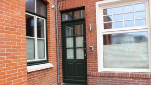 A brick house with a green door, a window with blinds, and a small porch area. - Altstadt Villa Wohnung 2 Hooge (Borkum)