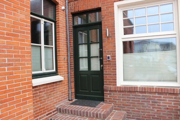 A brick house with a green door, a window with blinds, and a small porch area. - Altstadt Villa Wohnung 2 Hooge (Borkum)