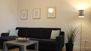 A living room with a black sofa, a coffee table with a decorative bowl, and a floor lamp. - Altstadt Villa Wohnung 2 Hooge (Borkum)