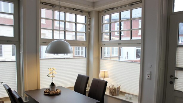A dining area with a table and chairs, large windows, and a pendant light. - Altstadt Villa Wohnung 2 Hooge (Borkum)