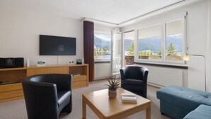 A modern living room with a flat-screen TV, two black armchairs, a wooden coffee table, and a blue sofa. - Allod Park Haus C 701 by Interhome (Davos)