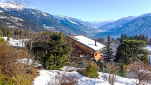A wooden cabin with a snow-covered roof, surrounded by trees and mountains. - Chalet Aglaia by Interhome (Crans-Montana)