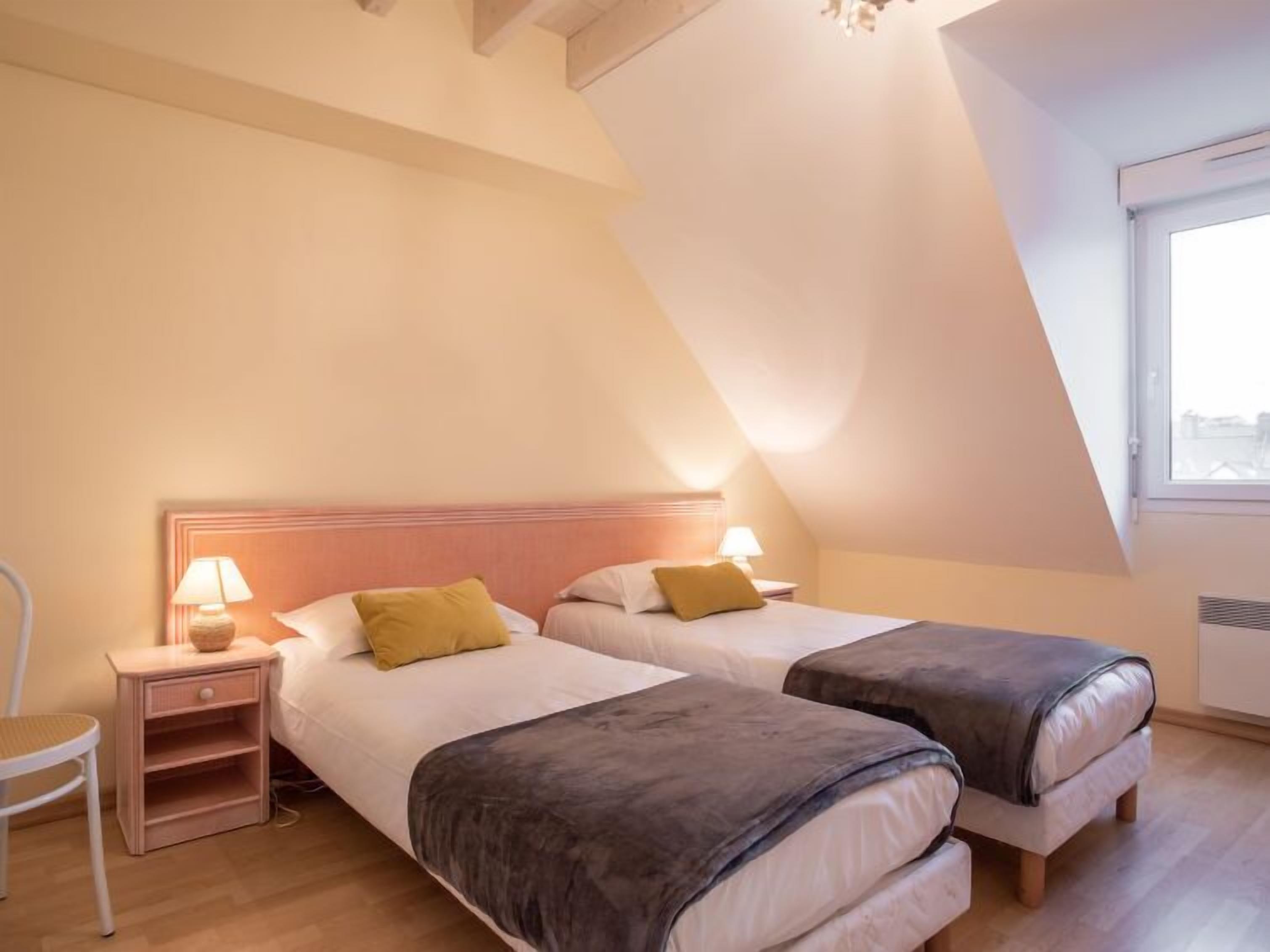 Une chambre avec deux lits, une table de chevet, une chaise et une fenêtre.