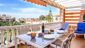 Ein Balkon mit einem Tisch, gedeckt für das Frühstück, darunter Orangen, Tomaten und eine Flasche Olivenöl.