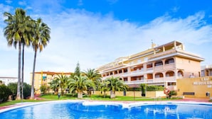Ein Hotel mit Pool, Palmen und einem Gebäude im mediterranen Stil.