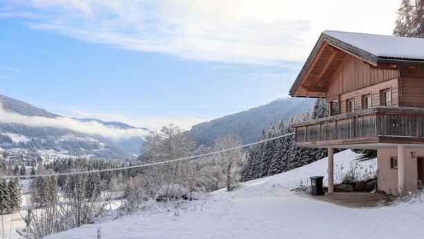 Een houten chalet met een balkon, tegen een besneeuwde berg als achtergrond.