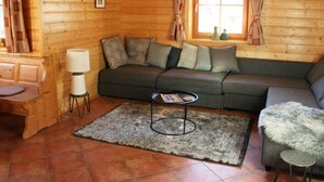 Een gezellig blokhutinterieur met een bank, een eettafel, een lamp en een raam met gordijnen.