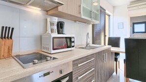 Een moderne keuken met een inbouwmagnetron, fornuis en spoelbak. Op het aanrecht staan een koffiezetapparaat en een broodrooster.